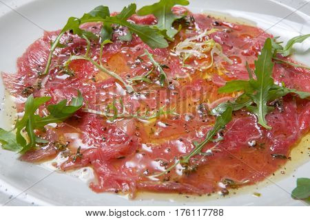 Beef Carpaccio Garnished With Fresh Arugula On White Plate