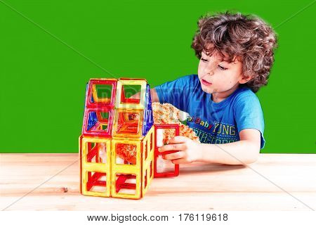 The amusing curly-headed kid plays with the cat who has got into the house through open doors. On a green background.