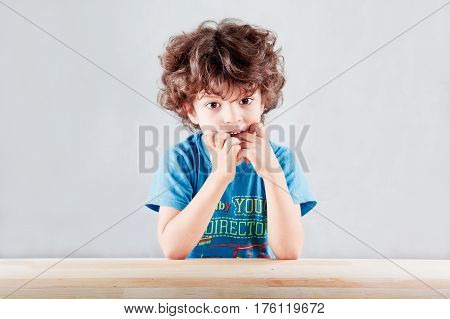 The lovely curly-headed kid in a blue t-shirt having thrust fingers listens spellbound in the camera. On a gray background. Close up.