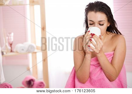Young woman with wet hair covered with pink towel relaxing after massage at spa salon