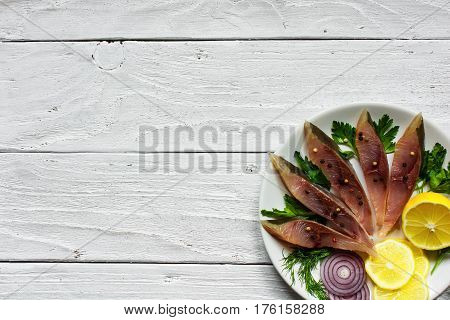 salted fish fillet with herbs lemon and spices in a plate on white wooden background with copy space. top view
