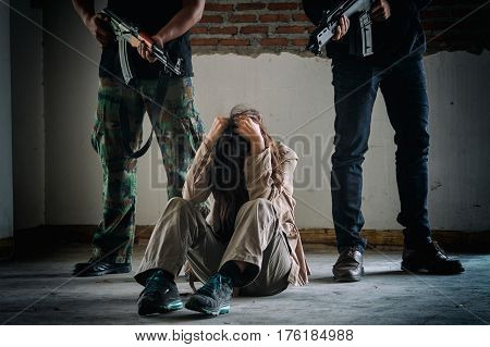 Kidnapper and victim. businesswoman sitting at the floor while two man aiming her with gun