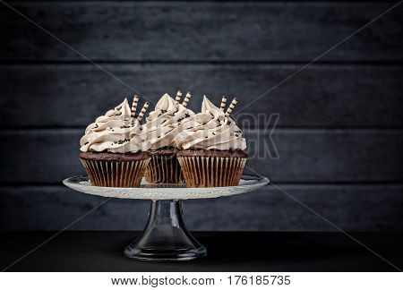 Three chocolate cupcakes with buttercream icing on a cake stand