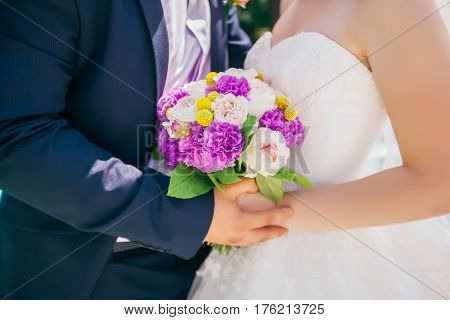 Newlyweds holding delicate and tender marriage bouquet in purple and pink colours with green petals