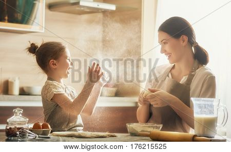 Happy loving family are preparing bakery together. Mother and child daughter girl are cooking cookies and having fun in the kitchen. Homemade food and little helper.