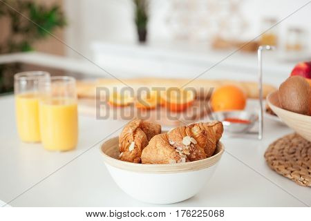 Plate of tasty cookies with chocolate crumbs, croissant, baget, bananas, apples, persimmon, orange and orange juice on white table.