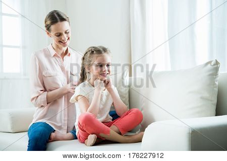 Smiling Mother Pleaching Daughter's Hair In Braids At Home