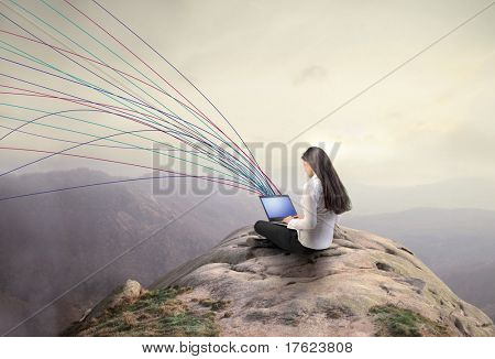 Woman using a laptop from a rock