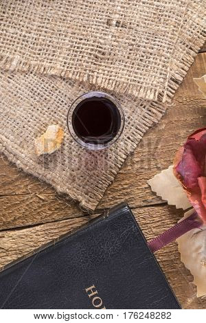 Taking Communion. Cup of glass with red wine bread and Holy Bible on wooden table close-up.