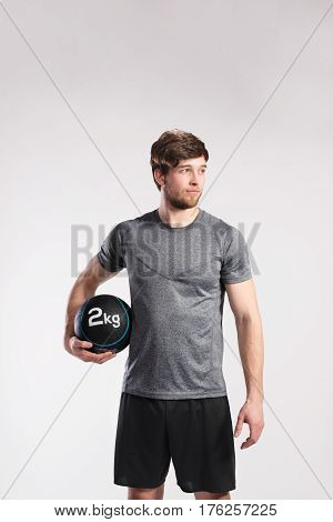 Handsome hipster fitness man in gray t-shirt holding medicene ball. Studio shot on gray background.