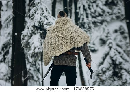 Strong Viking Warrior With Mohawk Haircut And Wolf Pelt Armor Holding Axe And Walking In Winter Wood