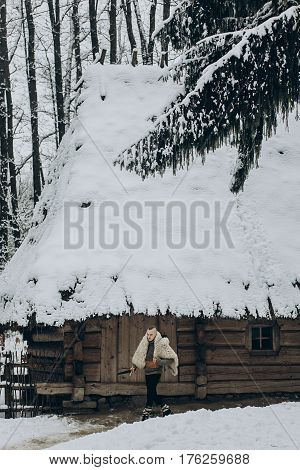 Strong Viking With Sword And Wolf Pelt Walking Towards Historical Wooden Building In North Woods In