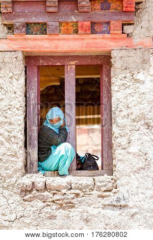 Hemis, India - June 29, 2012: Lonely covered with shawl young woman sitting in a windows span watching a religious masked and costumed Cham Dance Festival of Tibetan Buddhism in Hemis monastery India.