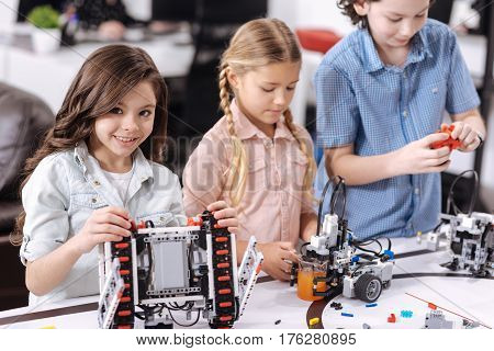 Realizing our science project. Charismatic delighted charming school children sitting at school and testing cyber devices while having science lesson