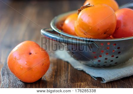 Fresh Persimmon On Wooden Table And Persimmons On Collander.