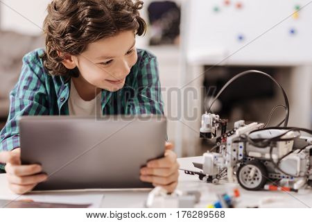Getting acquainted with new electronic friend. Outgoing delighted cheerful boy sitting at school and using digital gadget while studying and expressing joy