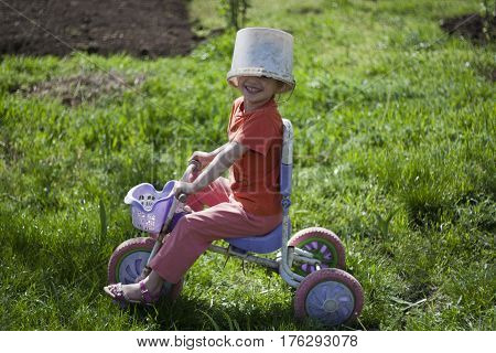 Cute girl playing outdoors with a bike and an old bucket