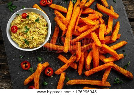 Healthy Homemade Baked Orange Sweet Potato Fries with guacamole, salt, pepper on stine, stone board.