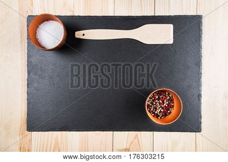 multicolored peppers peas and salt in a clay cup on a slate board wooden kitchen spatula top view