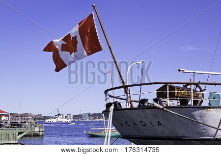 Halifax, Nova Scotia, September 23, 2015 -- Wide view of the back of a boat called the Acadia with a large Canadian flag flowing in the wind in Halifax Harbor with other boats and the ferry background on a bright sunny day in September in Halifax, Nova Sc