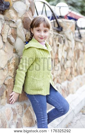 The little girl is standing by the stone wall