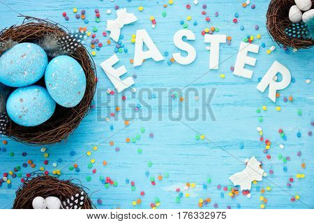 Easter background with blue and white eggs in nest butterfly and sugar sprinkles on a blue table top view with copy space Happy Easter concept