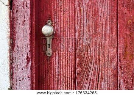Closeup of old red-stained, very grainy wooden door and silver doorknob with keyhole