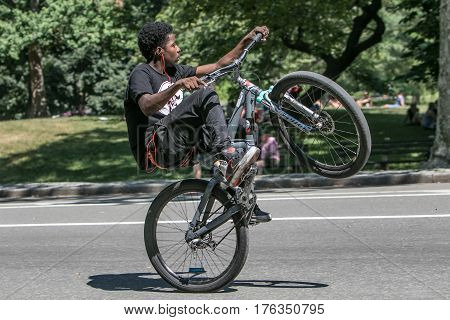 New York June 25 2016: A youth is riding his bicycle on one wheel in Central Park.