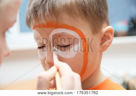 Make up artist making tiger mask for child.Children face painting. Boy painted as tiger or ferocious lion. Preparing for theatrical performance. Boy actor playing role. Tiger mask face