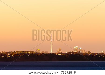 Distant skyline of Auckland City New Zealand with Sky Tower illuminated in twilight dusk after sunset