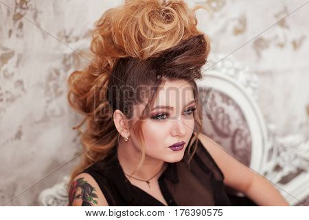 Fashion shiny makeup. Beauty woman with mohawk hairstyle. Blonde sexy model girl with long hair, long eyelashes, perfect skin. Creative unusual mohawk hairstyle. Skincare concept, model head. Rock style. Lady with tattoo