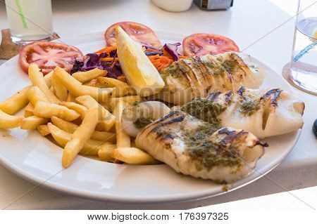 Grilled octopus. Grilled squid served with french fries and lemon and salad.