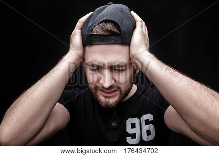 Frustrated young brunette man in black shirt with headache on black background. terrible migraine