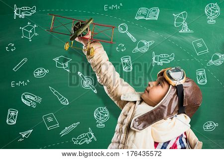 Happy Indian or asian boy kid playing with toy metal airplane against green chalk board with doodles drawn everywhere in the background - Kid and flying or ambition concept