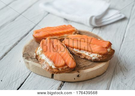 Sandwiches with smoked salmon and cream-cheese on a white wooden table. White napkin at the background