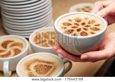 A lot of cups of coffee and a plate with a fire. Cappuccino coffee. A cup of latte, cappuccino or espresso coffee with milk put on a wood table. Drawing the foam milk on top.