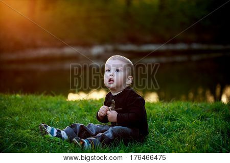 Little Boy Sits In The Evening On The Green Grass In The Park. Bila Tserkva. Park Aleksandriya. Ukra