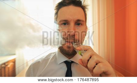 Vape. Young Funny White Businessman With Beard And Mustache Emits Puff Of Steam From The Electronic