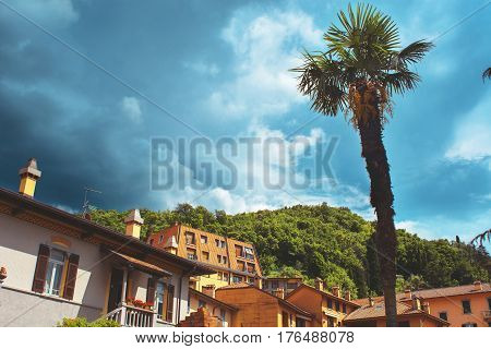 Beautiful toned cityscape of italian Varenna city with building big palm green valleys and dramatic sky before the rain