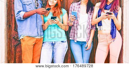 Group of teenagers texting mobile phone messages leaning against urban wall - Row of best student friends using smartphone wearing summer trendy clothing