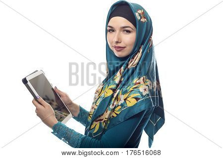 Female wearing a green hijab reading news online on a tablet or social networking via mobile device. She is isolated on a white background. The conservative outfit is associated with muslims and middle eastern culture.