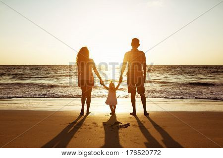 Family of father mother and daughter stands on background of sunset sea. Three silhouettes of happy people