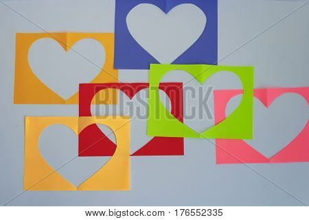 On a white background colored sheets are arranged in random order. On each of them a symbol of the heart is carved.