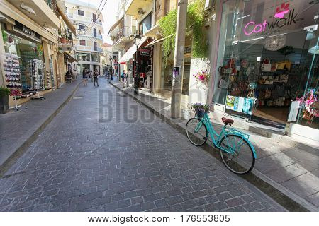 Rethymno Island Crete Greece - June 23 2016: Green colored bicycle with basket with purple flowers is parked on the narrow street of Rethymnon (part of Old Town) where there are a lot of small cafes and shops