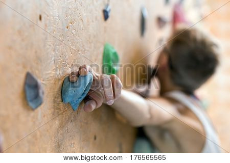 Young Female Climber in glasses on wall of indoor climbing gym with focus on hand holding the hold face is blurred and unrecognisable