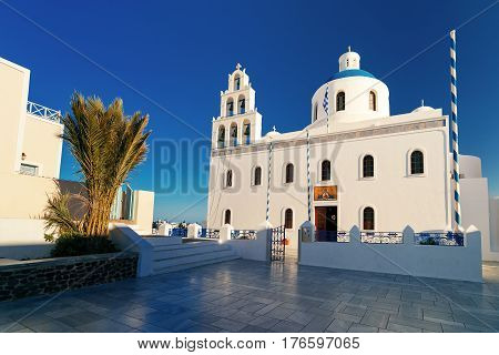 Picturesque square and white church of Panagia Platsani with blue dome in Oia or Ia on the island Santorini in the morning, Greece