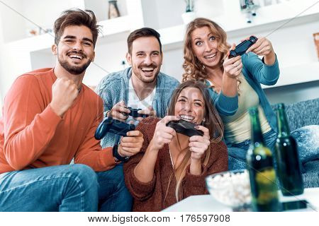 Happpy young friends playing video games at home.