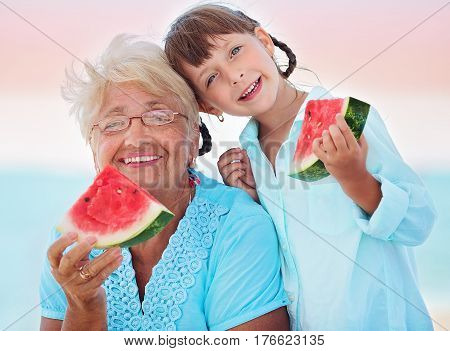 child and grandmother eating watermelon on the beach