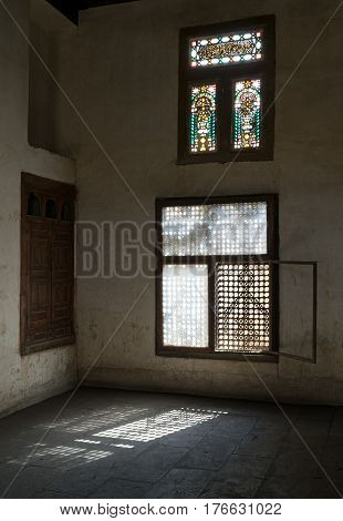 Cairo, Egypt - February 25, 2017: Old abandoned dark damaged dirty room with two wooden broken ornate windows covered by interleaved wooden grid (mashrabiya) at Zeinab Khatoun House