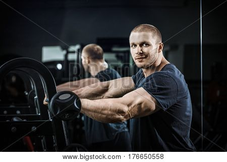 The bodybuilder after the training bodybuilder with pumped hand smiling in poses the weightlifter demonstrates his biceps powerlifting man strains the biceps pumped-up body of a huge.